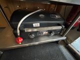 un barbecue à gaz posé sur une étagère métallique près d'une fenêtre