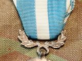 an old silver medal with a blue and white ribbon and a silver medal