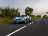the blue sports car is driving down the road on the side of the road