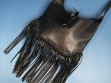 a black purse with fringes hanging from it ' s side against a blue sky