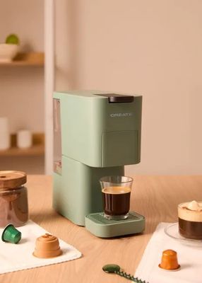 une cafetière verte posée sur une table, à côté d'une tasse de café