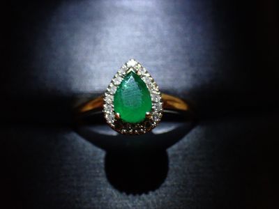 une bague sertie d'une émeraude et de diamants repose sur une surface noire