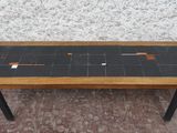 une petite table avec un plateau en carrelage noir posée sur un sol en briques