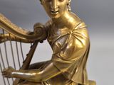 a gold statue of a woman playing a harp on a marble base