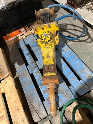 une perceuse jaune et noire posée sur une palette, à côté d'un tuyau vert