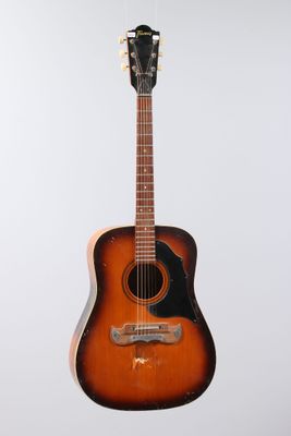 an old guitar hanging on a wall with a white background