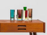 several different colored glass vases on a wooden table with a white background