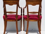 two wooden chairs with red upholstered cushions against a white wall