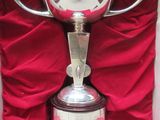 un trophée en argent dans un coffret rouge posé sur un tissu rouge