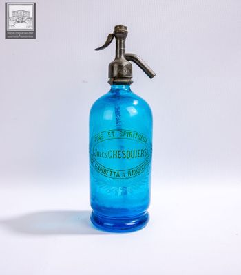 une bouteille en verre bleue munie d'une poignée en métal, posée sur une surface blanche