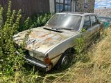 une vieille voiture est garée dans les herbes, à côté d'un bâtiment