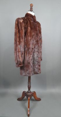un manteau de fourrure marron posé sur un mannequin, devant un fond gris