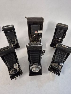 five old cameras are lined up on a white surface