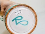 une personne tenant une tasse à café sur laquelle est peinte la lettre « r »
