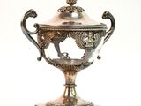 une coupe en argent posée sur un socle, sur une surface blanche