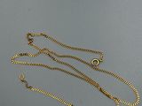 un gros plan d'un collier en or avec une chaîne, posé sur une surface grise
