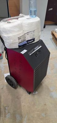 a red and black machine sitting on the floor next to a stack of toilet paper