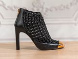 La chaussure à talons hauts noire et dorée est posée sur une table en bois