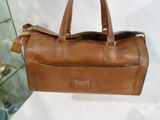 brown leather handbag sitting on a white surface next to a glass case
