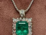 an emerald and diamond pendant on a brown velvet surface