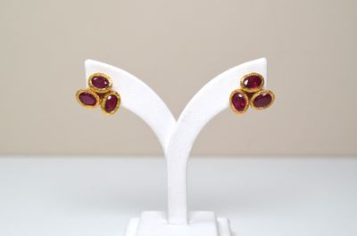 une paire de boucles d'oreilles en rubis et or, posée sur un socle blanc