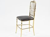 a gold metal chair with a black leather seat on a white background