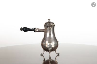 une cafetière ancienne en argent posée sur une table en verre, avec une poignée noire