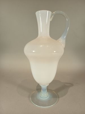 a white glass vase with a handle on a table
