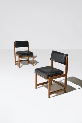 une paire de chaises en cuir noir et en bois posées sur une surface blanche