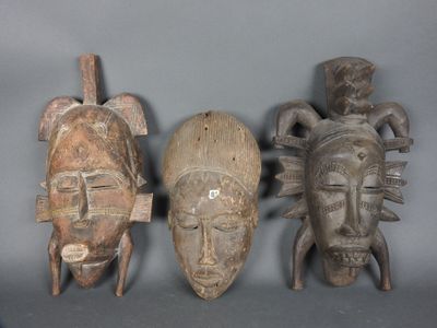 trois masques en bois sculptés sont posés sur une surface grise