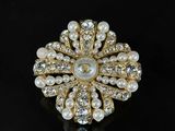 a close up of a pearl and gold broochle on a black surface