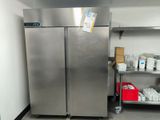 stainless steel refrigerators in a commercial kitchen with a shelf full of food