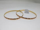 two gold bracelets with engraved designs on them sitting on a white surface