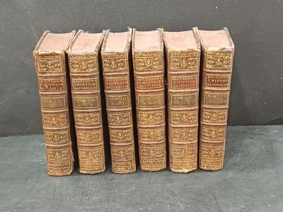 six old books are lined up on a black surface
