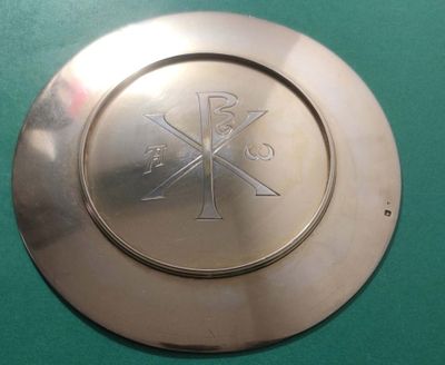une assiette en argent ornée d'une croix sur un fond vert
