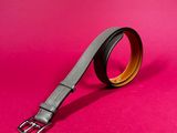 a black and brown belt with a metal buckle on a pink background