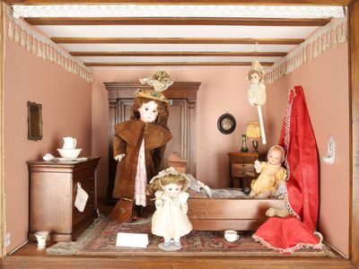 une maison de poupées avec des poupées à l'intérieur et une poupée assise sur le lit