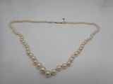 un collier de perles blanches avec un fermoir en or sur fond blanc