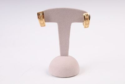 une paire de boucles d'oreilles dorées posées sur un socle blanc, sur fond blanc