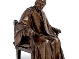 bronze statue of a man sitting on a bench with his feet crossed