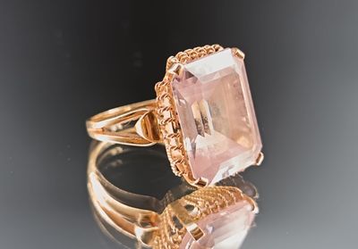 une photo d'une bague sertie d'une pierre rose, posée sur une surface réfléchissante