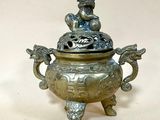 un petit pot en métal orné d'une statuette