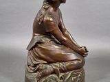 bronze statue of a woman sitting on a rock with her legs crossed