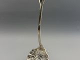 une cuillère en argent avec un manche en forme de feuille, posée sur un socle transparent