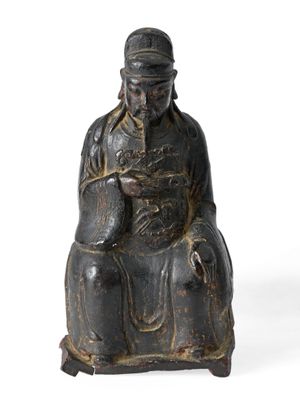 une vieille statue représentant un homme assis sur une chaise, coiffé d'un chapeau