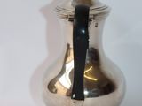 a silver coffee pot with a black handle on a white table