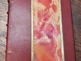 an old book with a red cover and gold trim on a wooden table