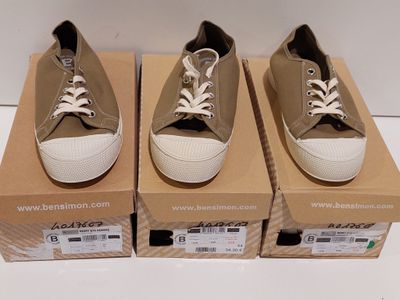 trois paires de chaussures sont posées sur des cartons, sur une surface blanche