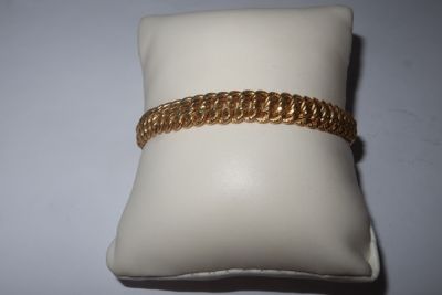a close up of a gold bracelet on a pillow on a white surface