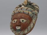 un masque en bois posé sur un socle en métal, sur fond gris